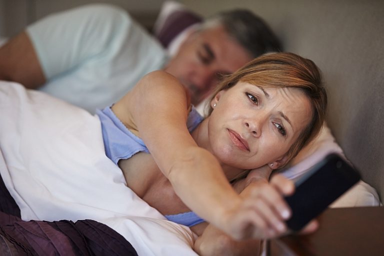 Woman lying awake in bed looking worried after a poor night's sleep while her partner sleeps beside her