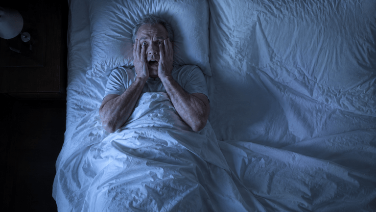 Frightened man awake in bed after a nightmare, representing trauma-related nightmares, PTSD sleep problems, and EMDR treatment