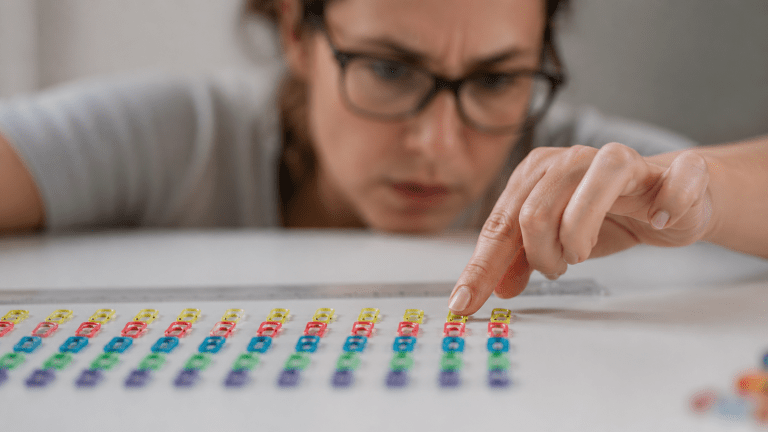 A tense woman carefully arranging colorful paper clips in perfect rows to represent perfectionism, rumination, and insomnia